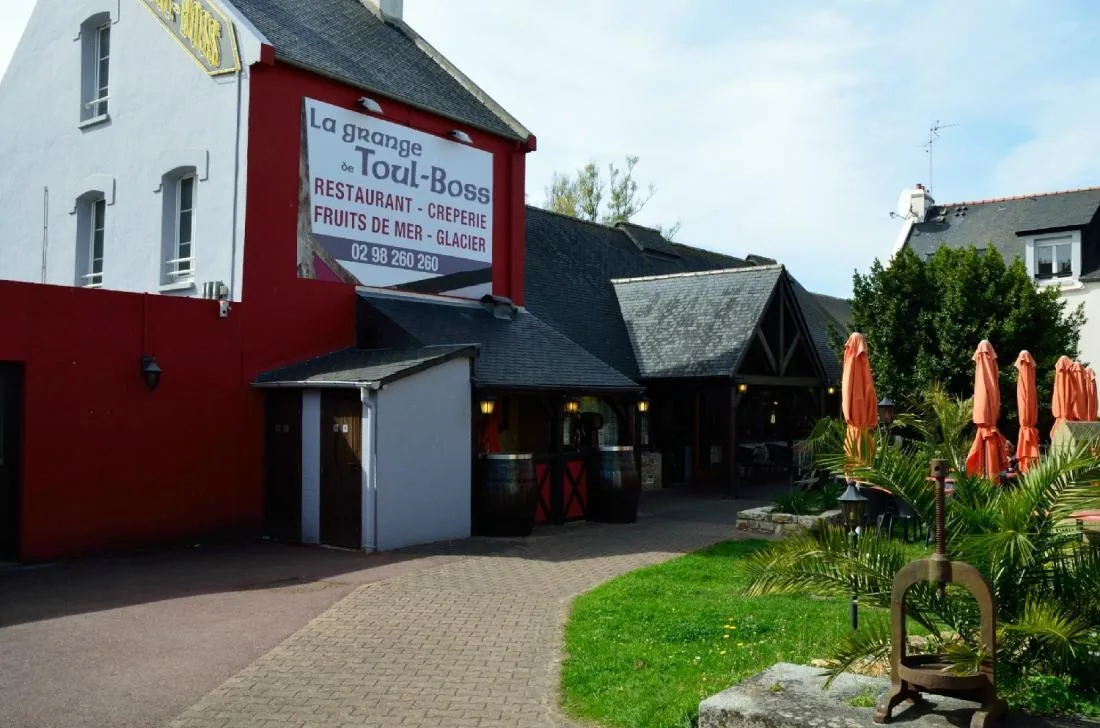 La façade de La Grange de Toul Boss à Morgat, son enseigne et sa terrasse avec parasols orange.